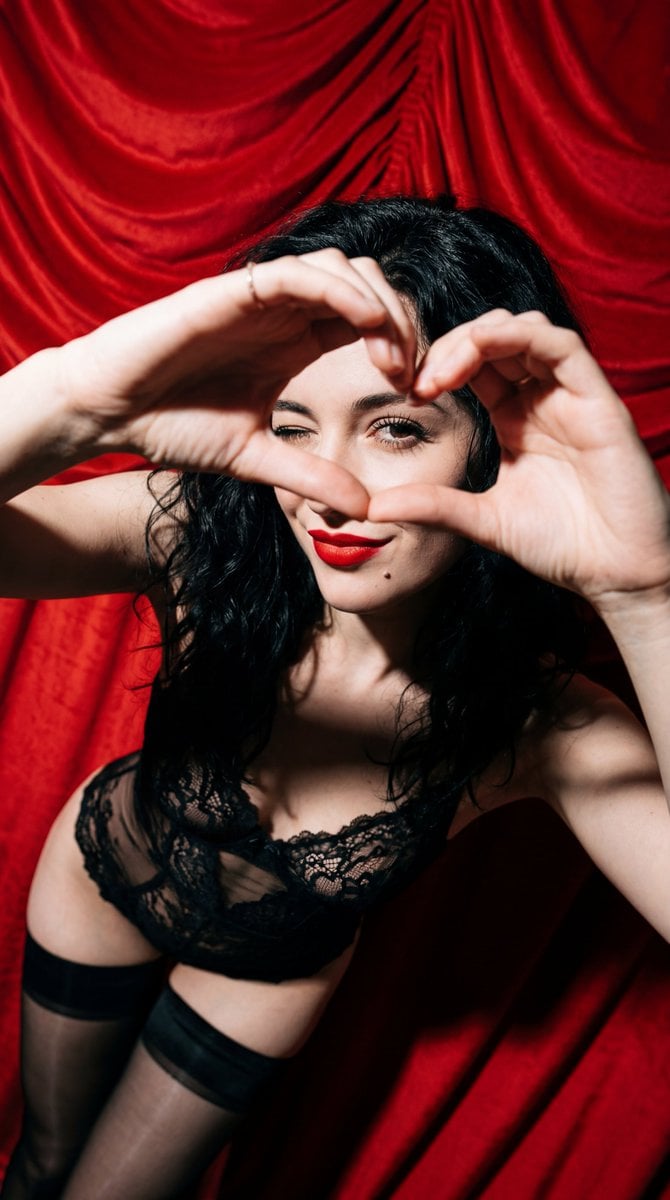 Subject: A young woman with wavy, tousled jet-black hair. She has a flirtatious expression with a subtle wink, crimson l