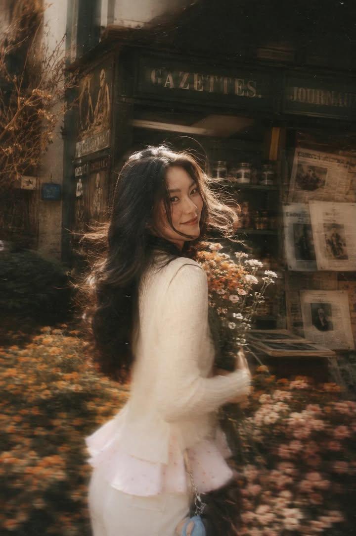 A beautiful young woman with long dark flowing hair holding a bouquet of soft pink roses, turning back and looking at th